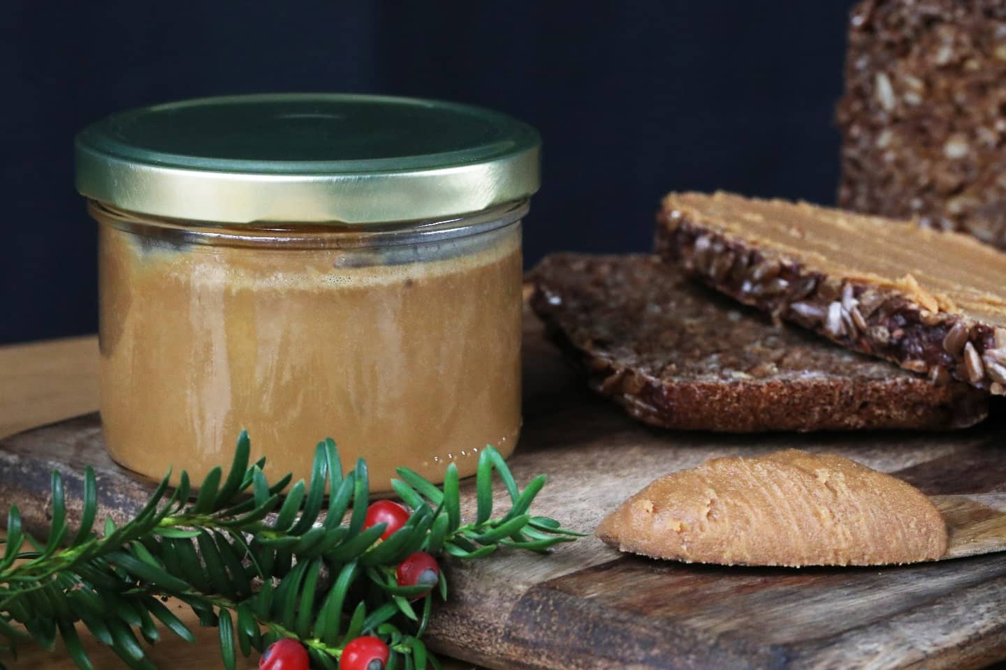 Pot de pâte à tartiner au chocolat et au café sur une petite planche en bois avec des branches de sapin de Noël et du pain complet.