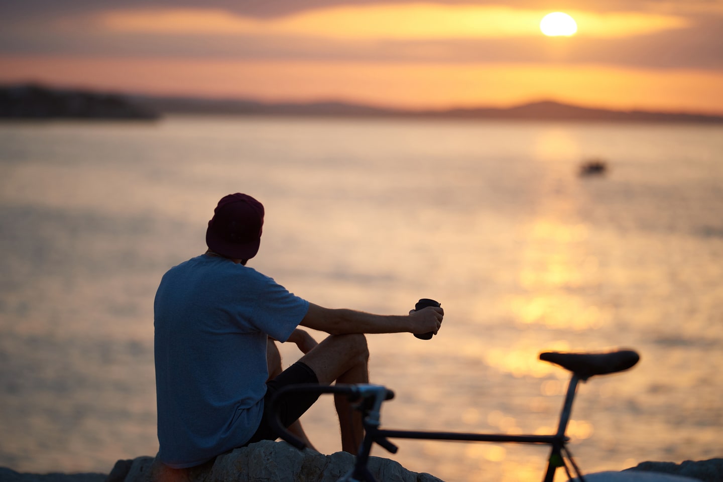 Une personne est assise sur un rocher et regarde le coucher de soleil