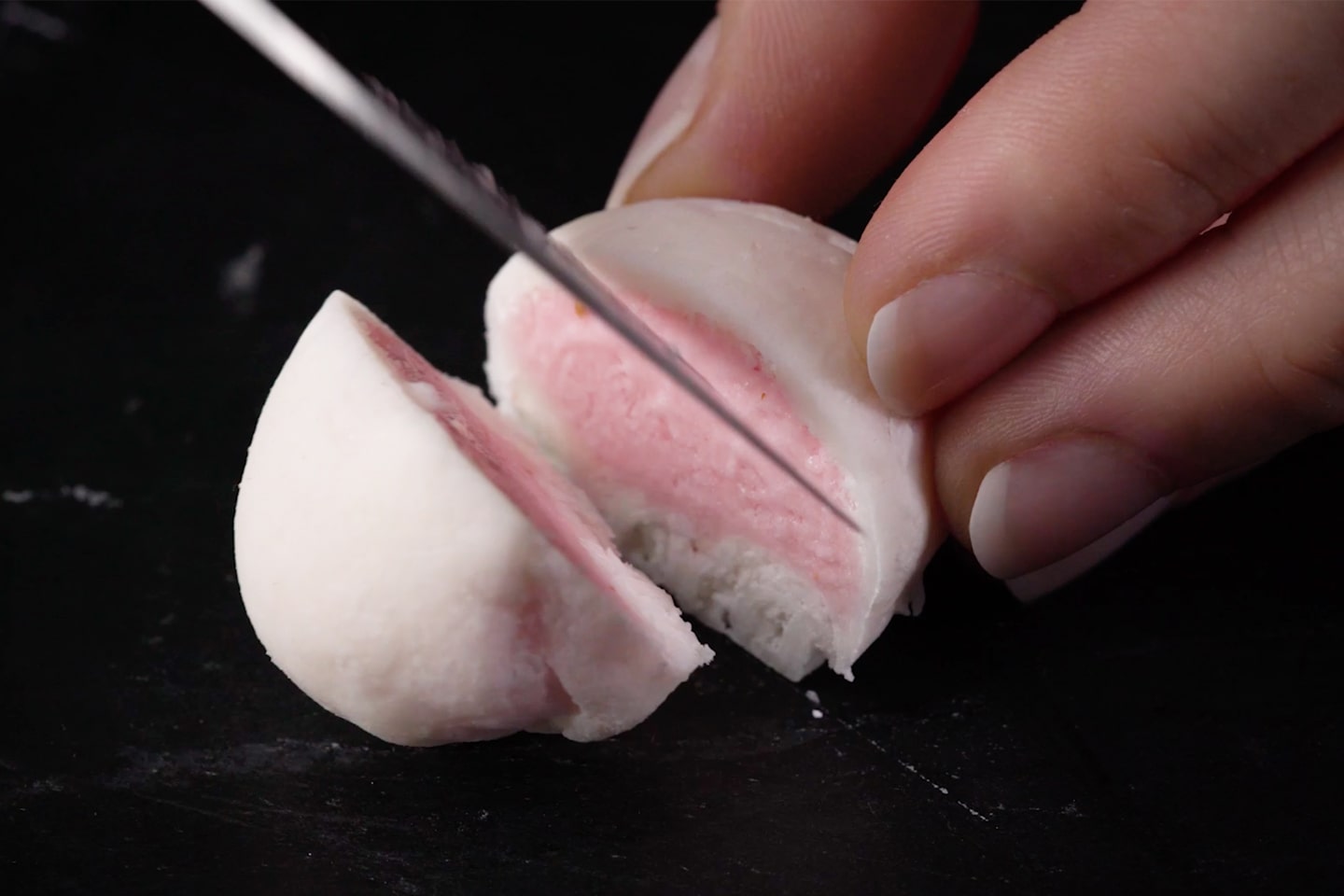 Iemand snijdt mochi-ijsbolletje met aardbeienvulling in tweeën Recept voor mochi-ijslolly's Café Royal recept