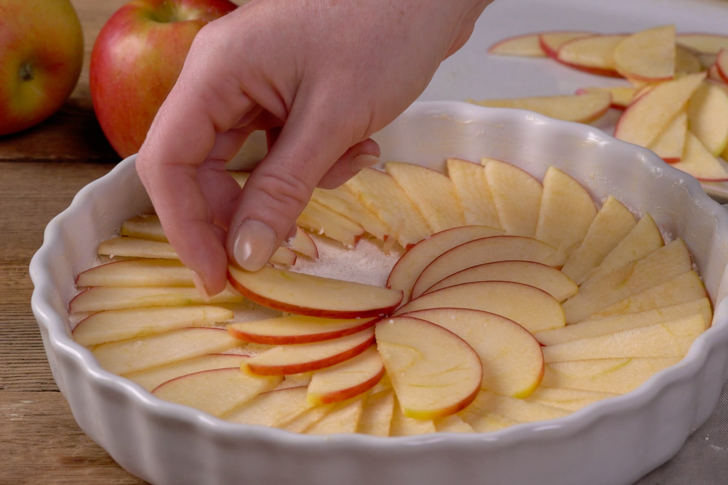 Vrouwenhand legt appelschijfjes in een decoratief patroon in een bakvorm voor een apple crumble met koffie
